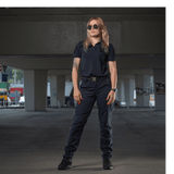Kvinde iført M-Tac Bukser Aggressor Dame Flex under en viadukt, ideel til træning eller arbejde, beskytter mod vand og snavs.