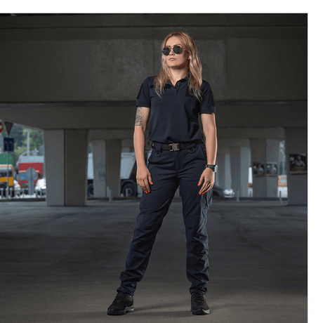 Kvinde iført M-Tac Bukser Aggressor Dame Flex under en viadukt, ideel til træning eller arbejde, beskytter mod vand og snavs.