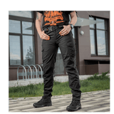 Model iført M-Tac Bukser Aggressor Dame Flex foran en bygning, sort og taktisk design, velegnet til forskellige udendørs aktiviteter.