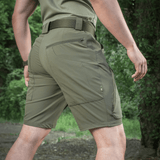 M-Tac Shorts Rubicon Flex i mørk oliven med cargolommer til sommerbrug og maksimal bevægelsesfrihed, set bagfra i udendørs omgivelser.