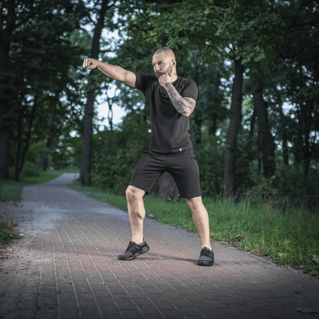 Mand i skov iført M-Tac Shorts Casual Fit Cotton, viser bevægelighed og stilrent design på en sti omringet af træer i naturen.