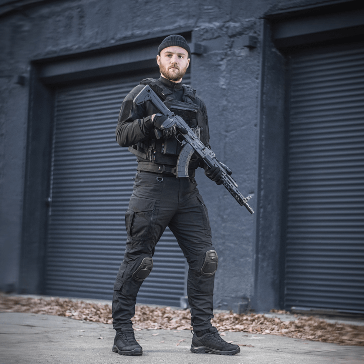 Mand iført M-Tac Bukser Army NYCO Extreme i sort udendørs setting med skydevåben, komfort og funktionalitet demonstreret