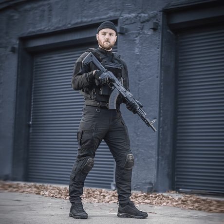 Mand iført M-Tac Bukser Army NYCO Extreme i sort udendørs setting med skydevåben, komfort og funktionalitet demonstreret