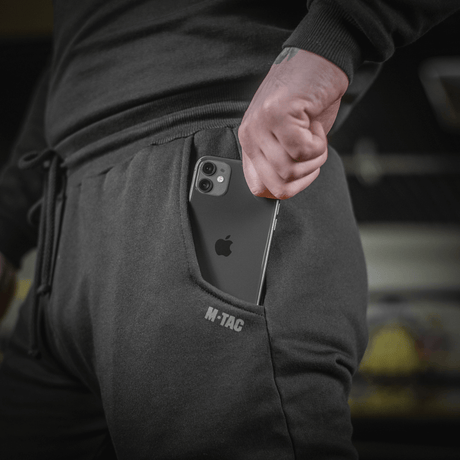 Person iført M-Tac Bukser Cotton Classic med smartphone i sidelomme, sportstøj i 100% bomuld med komfort og bevægelsesfrihed.