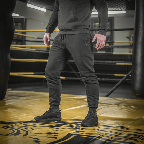 Mand iført M-Tac Bukser Cotton Classic i træningscenter, fremhæver alsidige sportbukser med komfort og stil.