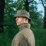 Mand iført M-Tac Panama Rip-Stop hat i skovmiljø, med ventilationshuller og camouflagestropper for optimal anvendelighed og stil.