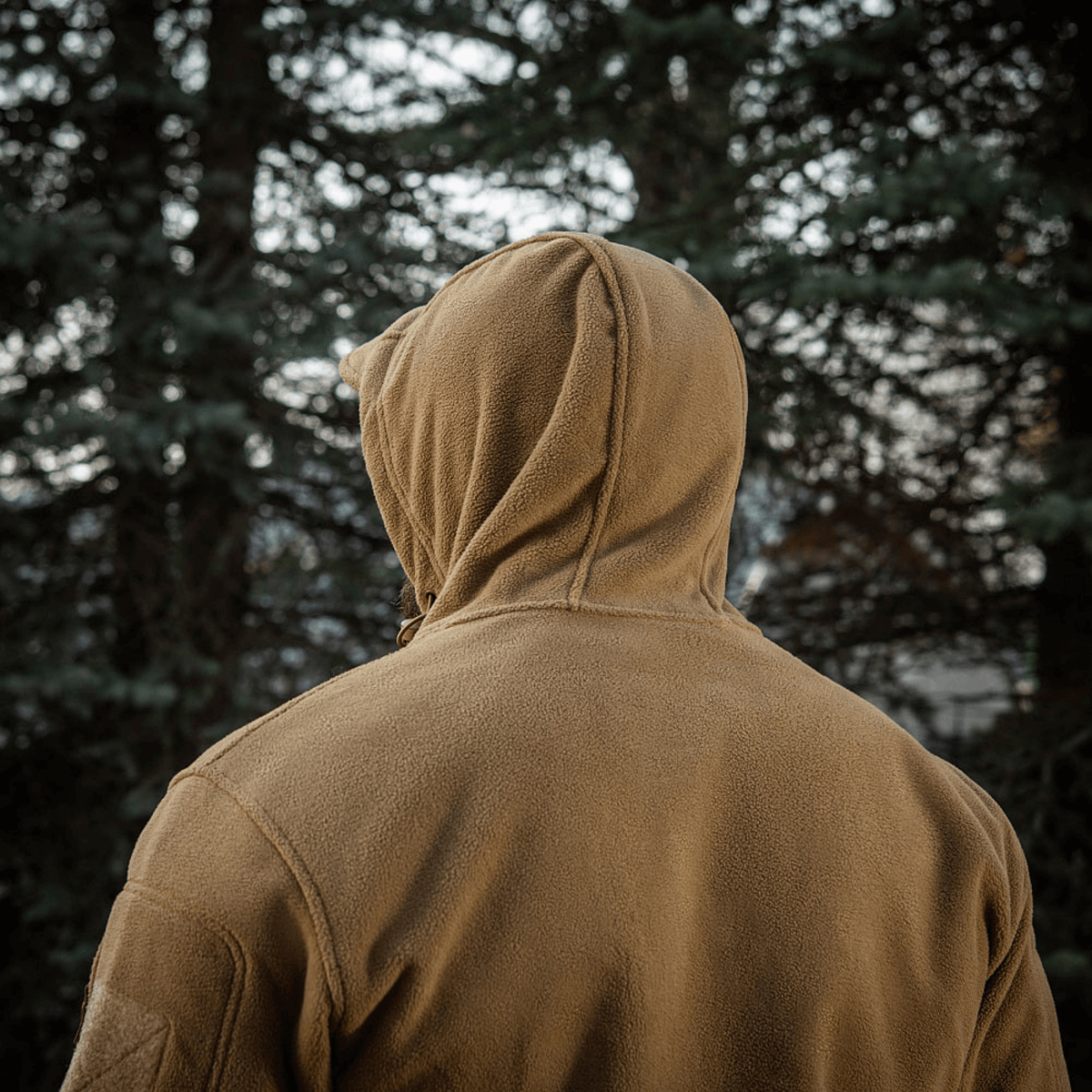 En person iført M-Tac Division Gen.II Windblock Fleecejakke foran skovbaggrund, ideel til beskyttelse mod køligt og koldt vejr.