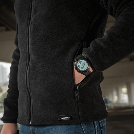 Person iført M-Tac Nord Polartec Fleecejakke med en digital ur under jakkeærmet, der viser temperaturen.