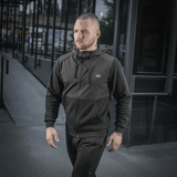 Mand iført sort M-Tac Pilgrim Bomberjakke går på gaden, fremhæver stilfuld og praktisk design, ideel til hverdagsbrug.