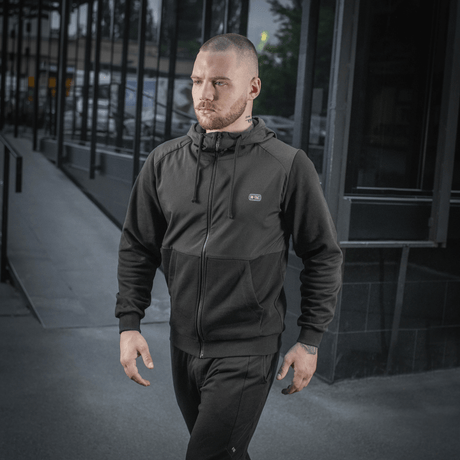 Mand iført sort M-Tac Pilgrim Bomberjakke går på gaden, fremhæver stilfuld og praktisk design, ideel til hverdagsbrug.