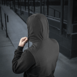 Person iført M-Tac Pilgrim Bomberjakke med hætte, set bagfra på en urban baggrund.