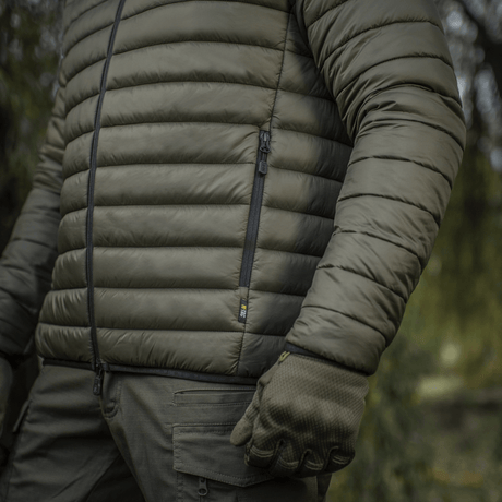 Mand i M-Tac Stalker Gen.III Jakke i skovmiljø, viser detaljeret syning og lynlås, perfekt til overgangssæsonen.