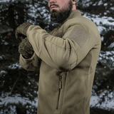 Mand iført M-Tac Combat Fleece Polartec Jakke i skov, fremhæver taktisk design og funktionalitet.
