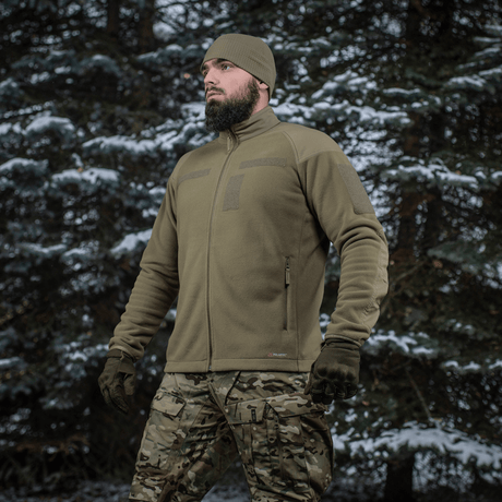 Mand iført M-Tac Combat Fleece Polartec Jakke i skovmiljø, viser jakken's funktionelle og taktiske design, ideel til udendørs brug.