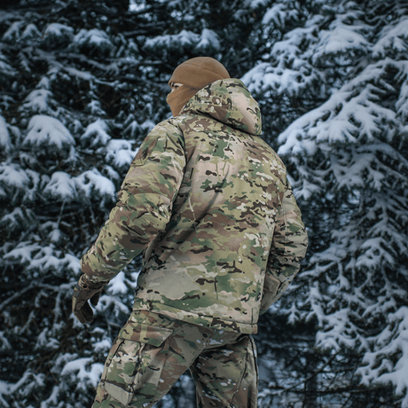 M-Tac Alpha Gen.IV Pro Primaloft Vinterjakke i snebeklædt skov med Multicam-design for ekstrem holdbarhed og koldbeskyttelse.