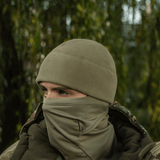 Person iført M-Tac Watch Cap Elite Fleece Beanie Hat Slimtex i natur, ideel til koldt vejr og taktisk brug med camouflagejakke.