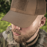M-Tac Baseball Cap Ripstop Elite Flex i brun med netpaneler, båret af en person i camouflage-tøj, set forfra udendørs.