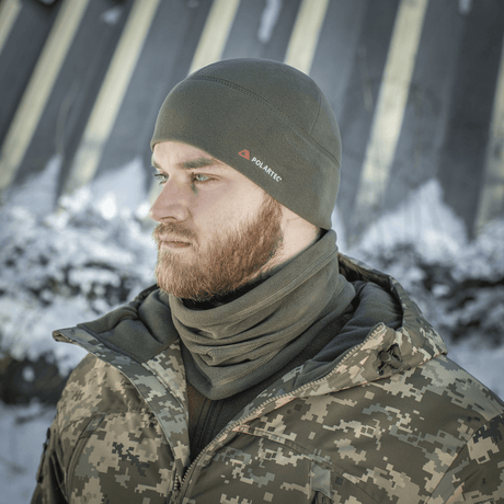Mand iført grå M-Tac Fleece Watch Cap Light Polartec hue i sneklædt landskab, bæret med camouflagetøj, perfekt til vintervejr.