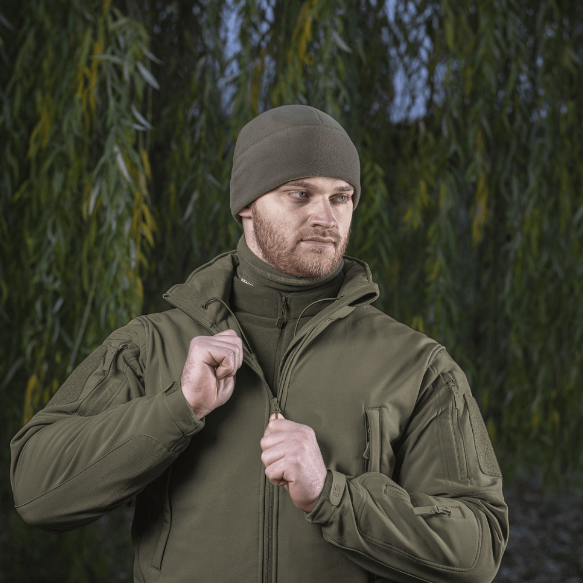 Mand iført M-Tac Fleece Polartec Watch Cap i skovmiljø, ideel til udendørs vinteraktiviteter og beskyttelse mod kulde og vind.