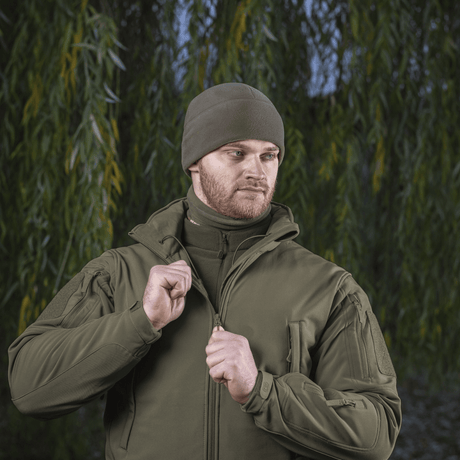 Mand iført M-Tac Fleece Polartec Watch Cap i skovmiljø, ideel til udendørs vinteraktiviteter og beskyttelse mod kulde og vind.