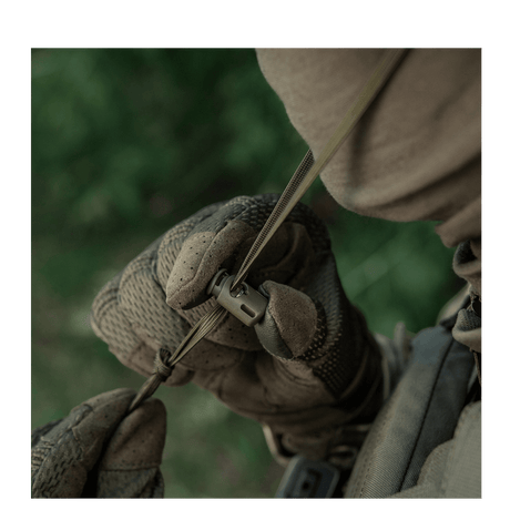 Person iført camouflagetøj justerer et spænde på en M-Tac Panamahat Gen. II Summer Flex i naturmiljø