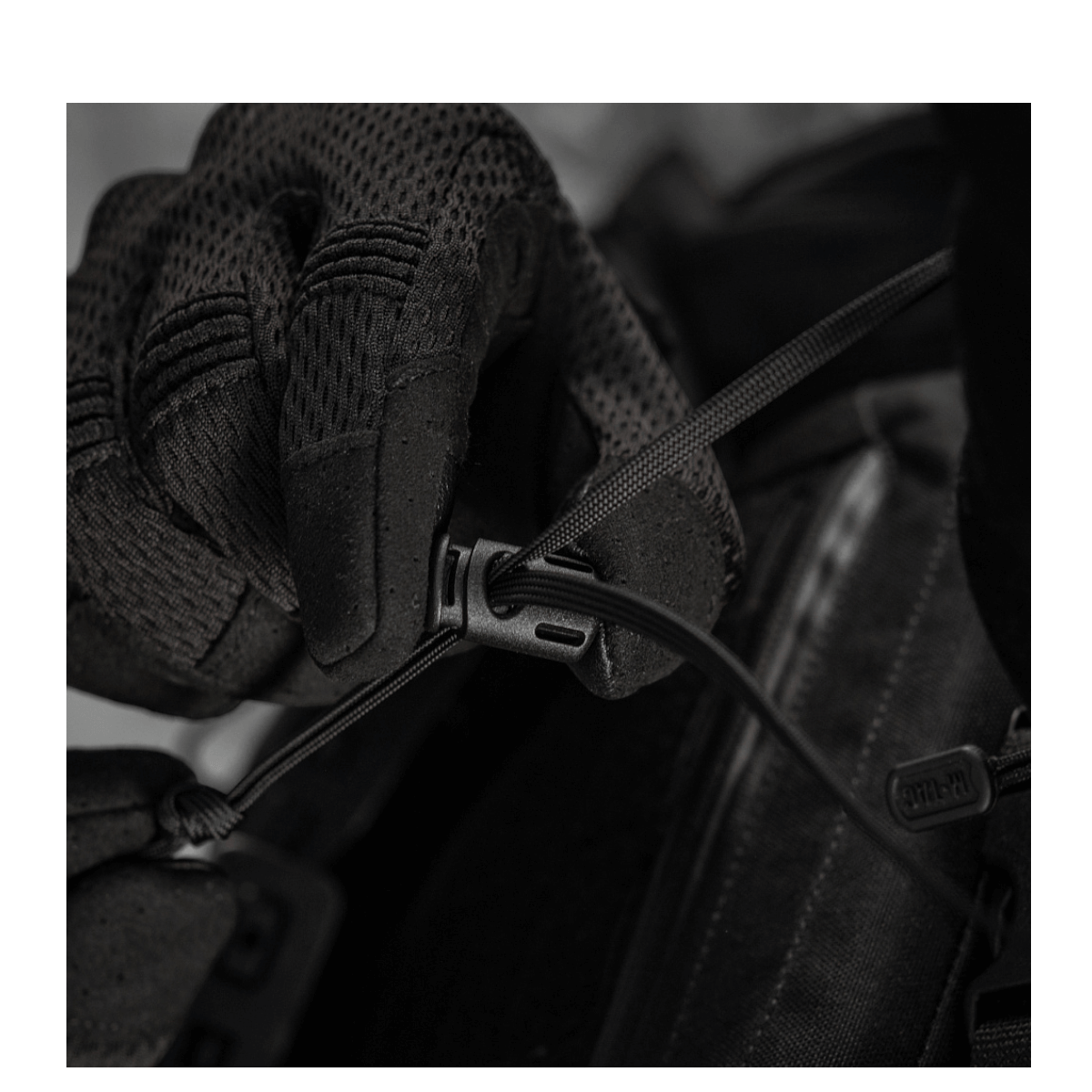 Næroptagelse af sort handske justerer en snøre på en M-Tac taske