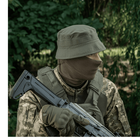 Soldat i camouflagetøj med M-Tac Panamahat Gen. II Summer Flex, holder riffel, omgivet af skov. Perfekt til sommerture og solbeskyttelse.