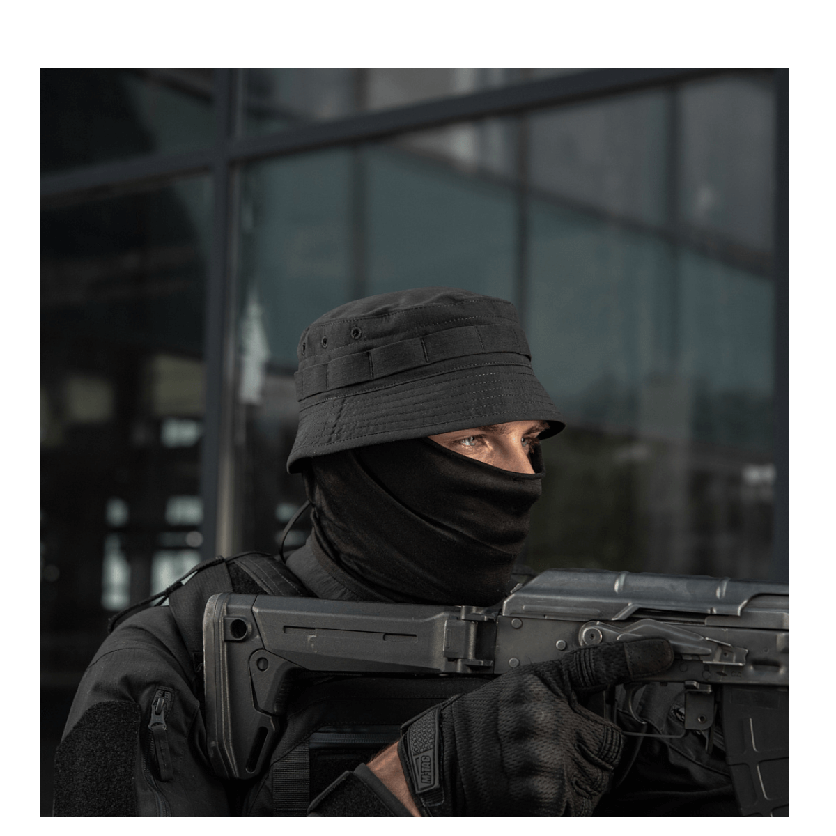 Person wearing tactical gear and holding a firearm, outdoors.