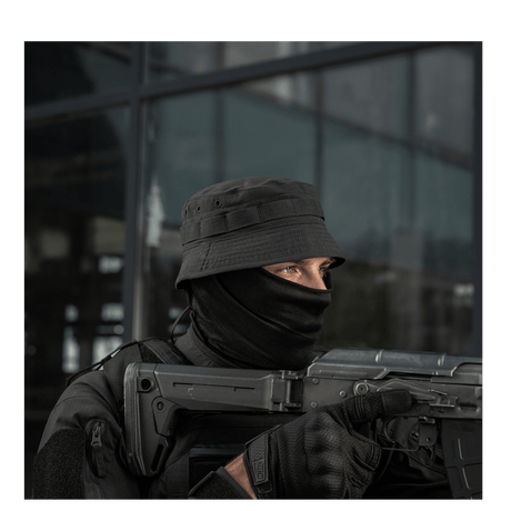 Person wearing tactical gear and holding a firearm, outdoors.