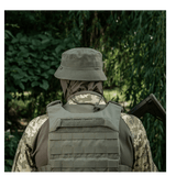 Person i camouflageuniform med hjelm og vest i skov.