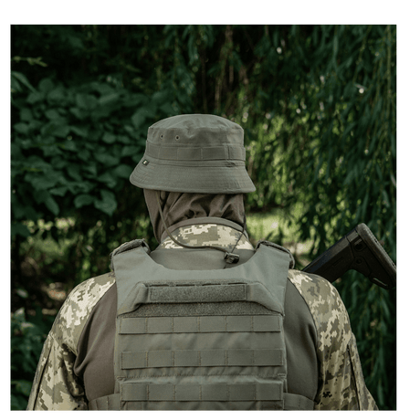 Person i camouflageuniform med hjelm og vest i skov.