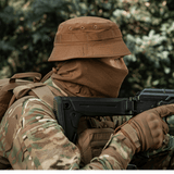 Person iført M-Tac Panamahat Gen. II Flex Rip-Stop i camoufleret tøj med våben baggrund af natur