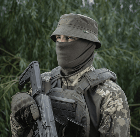 Person iført M-Tac Panamahat Gen. II Flex Rip-Stop med maskering, camouflageudstyr i skovmiljø.