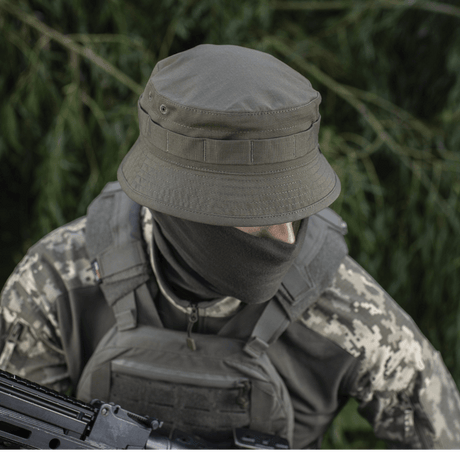 Person iført M-Tac Panamahat Gen. II Flex Rip-Stop i militært udstyr, viser slitstærk konstruktion og komfort i naturmiljø.