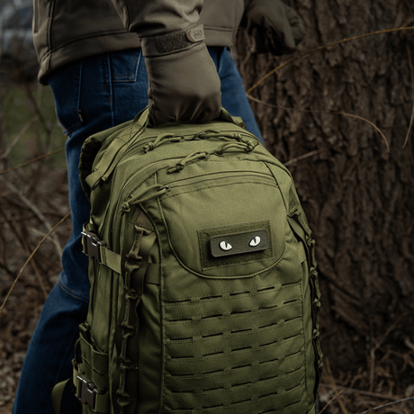 M-Tac Cat Eyes 3D PVC Patch på rygsæk i skov, ideel til taktiske og udendørs aktiviteter, reflekterende design, nem fastgørelse med Velcro.