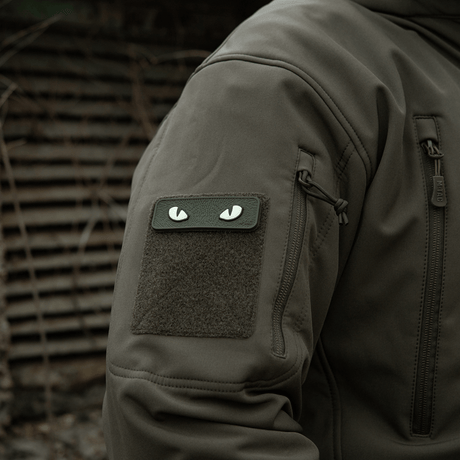 M-Tac Cat Eyes 3D PVC Patch på jakkeærme i taktisk miljø, viser lysreflekterende og fluorescerende design, fastgjort med Velcro.