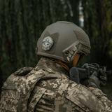 Soldat iført taktisk hjelme med M-Tac Patch Emoji #4 i skoven, PVC med 3D-effekt og Velcro, morale patch, 6.5 x 6.5 cm, holdbar og sjov.