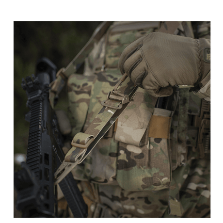 M-Tac Universal Våbenrem i brug på et camouflageudstyr, der letter håndtering af gevær og karabin. Ideelt til to-punkts og enkelt-punkts fastgørelse.