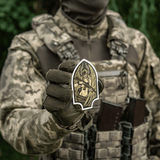 Soldat iført kamouflageuniform, der holder M-Tac Sticker Valkyrie, som viser en krigsgudinde med stiliseret hjelm og M4 gevær.