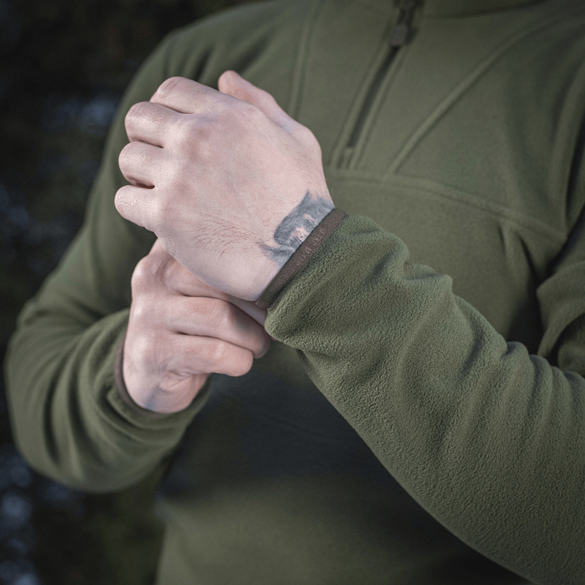 Person iført M-Tac Delta Polartec Fleecejakke justerer ærme i en udendørs setting.