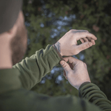 Mand justerer manchetten på en M-Tac Delta Polartec Fleecejakke i en skov, som viser jakkens funktionelle design og materiale.