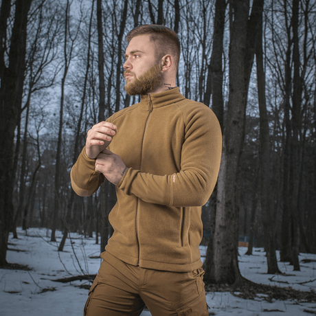 Mand iført M-Tac Polartec Sport Fleecejakke, står i skov med sne, demonstrerer jakken's komfort og funktionalitet i koldt vejr.