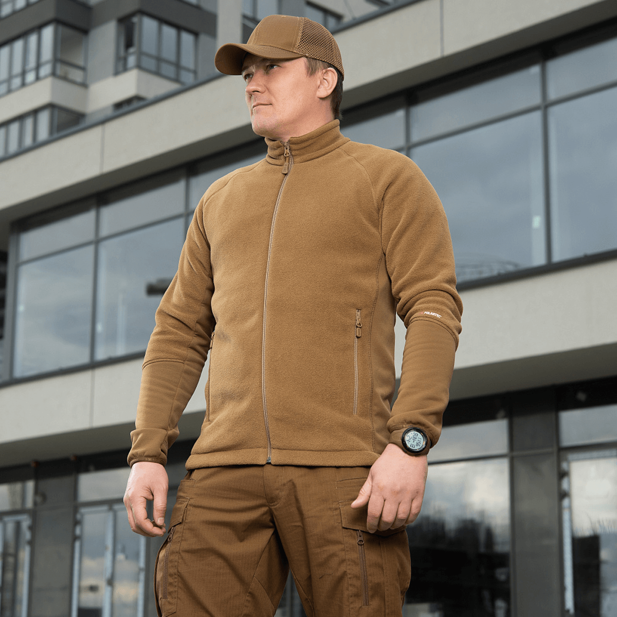 Mand iført M-Tac Polartec Sport Fleecejakke står foran moderne bygning, ideel til overgangsperioder og koldt vejr.