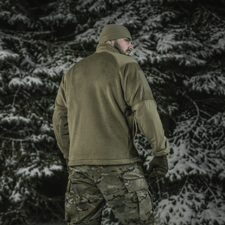 Mand iført M-Tac Battle Fleece Polartec Jakke i sneklædt skov, set bagfra med anatomisk pasform og camouflagebukser.