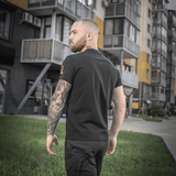 Mand bærer en M-Tac T-shirt Black Sea Expedition foran moderne bygninger