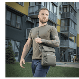 Mand med M-Tac Konvert Taske Elite i gråt bymiljø, bærende en moderne tablet-design taske lavet af holdbart Cordura materiale.