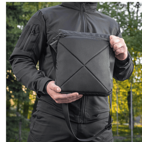 Mand holder M-Tac Konvert Taske Elite i sort, lavet af slidstærkt Cordura, med en justerbar skulderrem og tablet-design.