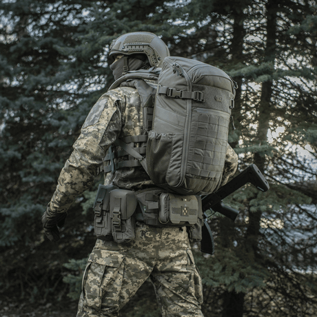 Soldat i skov med M-Tac Rygsæk Gen. II Elite – Small, med MOLLE-paneler og sidelommer, designet til sikker opbevaring og nem pakning.