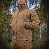 M-Tac Soft Shell Jakke i naturmiljø, viser jakke med indre polyuretan-membran og fleece-lag, ideel til beskyttelse mod vind og vejr.