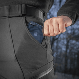 Person iført M-Tac Bukser Soft Shell Vinter med en telefon i lommen, fremhæver deres praktiske og funktionelle design til kolde klimaer.